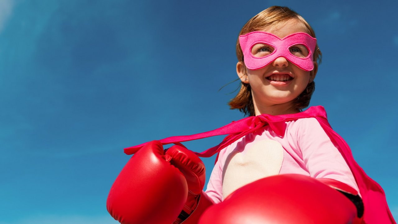 Ein Mädchen mit Superheldinnenbrille, Umhang und Boxhandschuhen.